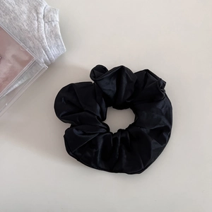 Detail of black satin scrunchie showing glossy fabric texture and pleated design