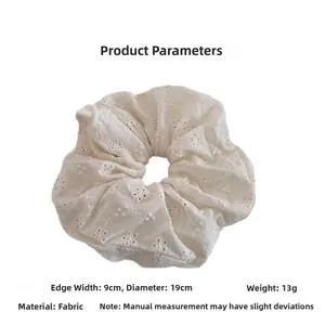 Detail view of a white lace scrunchie with floral embroidery showing 19cm diameter size