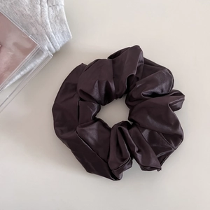 Detail view of large dark brown satin scrunchie with a glossy texture on beige background
