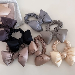Detail view of seven assorted satin bow scrunchies in elegant neutral earth tones