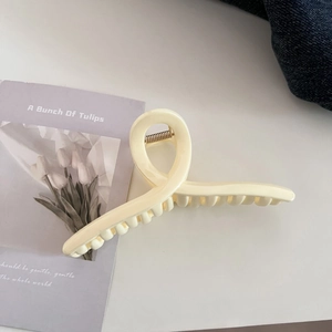 Detail of a large cream-colored hair claw clip with a minimalist twisted design and metal spring