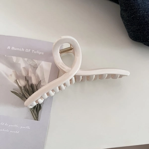 Close-up of a cream-colored twisted claw clip with glossy finish and gold metal spring