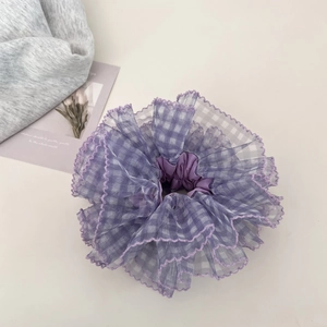 Close-up of purple plaid mesh scrunchie with layered ruffle edge on a soft fabric background