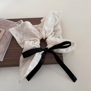 Close-up of white lace scrunchie with floral embroidery and black satin bow detail