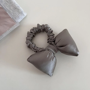 Close-up of a dark grey satin scrunchie with a large bow showing fabric texture