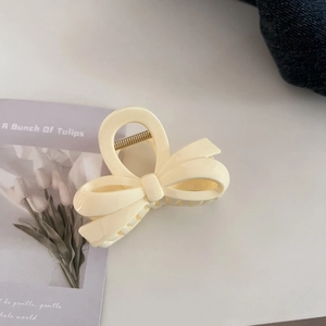 Macro detail of cream beige bow hair claw clip on tulip card and denim background