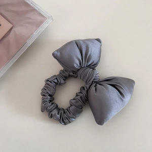Close-up of a grey satin bow scrunchie with silk luster on a light beige background