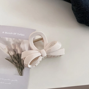 Close-up of a creamy beige ribbon bow hair claw clip with metallic spring components