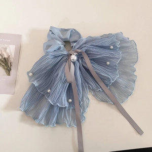 Détail d'un chouchou noeud en mousseline plissée bleu clair avec perles et rubans
