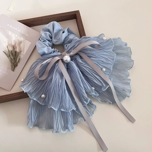 Détail d'un chouchou en mousseline plissée bleu clair avec nœud gris et perles