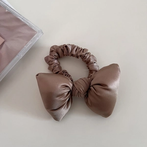Detailed view of large champagne satin bow scrunchie with silky pleated texture