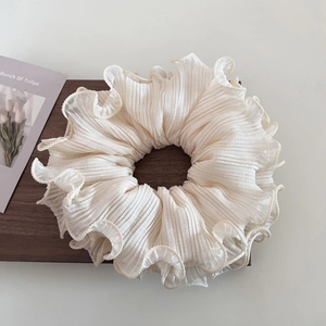 Elegant cream pleated chiffon oversized scrunchie with ruffled edges on wooden base