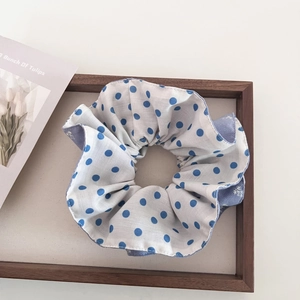 Detail of white scrunchie with blue polka dots and soft cotton texture on a wooden prop