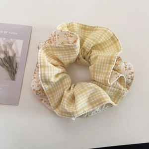Detail of a large scrunchie with yellow plaid and floral fabric on a white surface