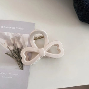 Detailed macro view of cream-colored bow hair claw clip with sturdy metal spring hinge