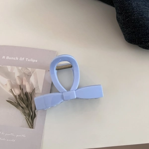 Detail shot of light blue bow-shaped hair claw clip with glossy finish on white table