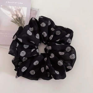 Detailed view of a black chiffon scrunchie with white polka dots on soft ivory backdrop