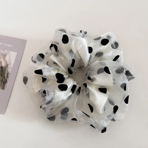 Close-up of double-layered white mesh scrunchie with black polka dots on light background
