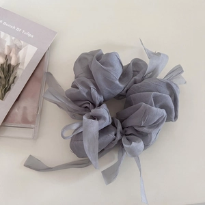 Macro detail of a grey tulle scrunchie with long ribbons on a minimalist cream surface