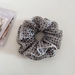 Detailed view of the purple floral fabric scrunchie with delicate ruffled edges texture