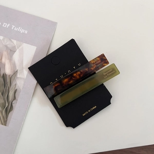 Close-up of tortoiseshell and matte green acetate hair clips on a minimalist card