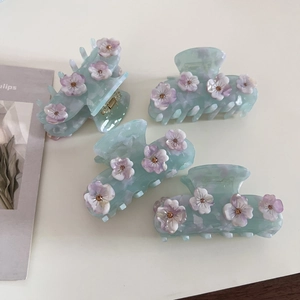 Dettaglio macro di pinze per capelli in acetato verde menta con fiori sfumati viola e strass