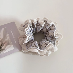 Detailed view of purple floral fabric scrunchie with double-layer white lace trim
