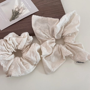 Detailed close-up of beige cotton linen scrunchies with floral embroidery and side label