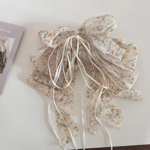 Détail d'une pince à cheveux en mousseline fleurie avec de longs rubans sur fond crème