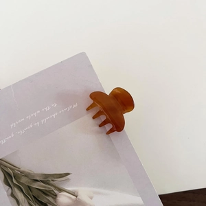 Close-up of small amber brown acetate hair claw clip on a minimalist aesthetic background