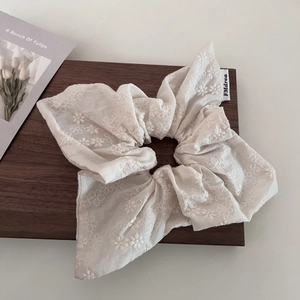 Macro detail of creamy white linen scrunchie with floral embroidery and FMdrea label