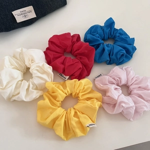 Gros plan de cinq chouchous en coton colorés avec texture plissée et étiquettes de marque
