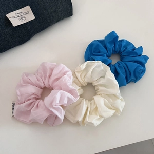 Lot de trois chouchous en coton en rose, crème et bleu sur un fond blanc épuré
