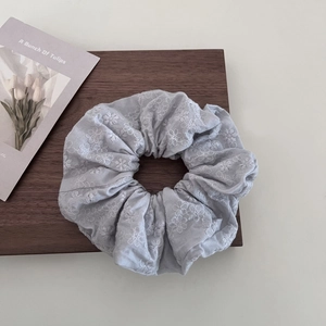 Detail of light blue linen scrunchie with white floral embroidery on a wooden background