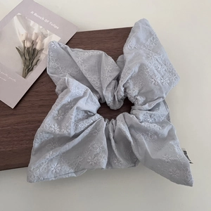 Detailed close-up of light blue linen scrunchie with white floral embroidery on wood