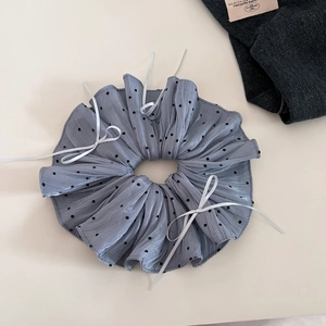Close-up of oversized light blue polka dot scrunchie with delicate white silk ribbon bow