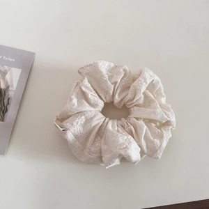 Detailed close-up of cream lace embroidery and soft fabric texture of the hair scrunchie