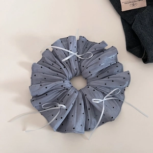 Close-up of a blue polka dot scrunchie with white ribbon bows on minimalist background