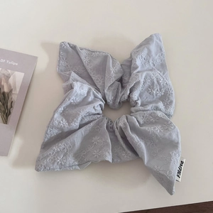 Close-up of lilac linen scrunchie with white floral embroidery and branded woven label
