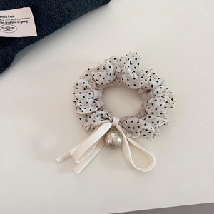 Close-up of a polka dot scrunchie with a satin bow and metallic pearl pendant