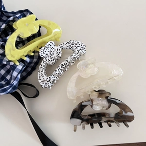 Detail view of four floral acetate hair claws in yellow, cow print, white and tortoise