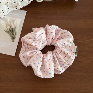 Close-up of pink floral scrunchie with lace edge and brand label on wooden surface