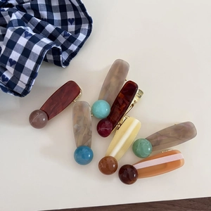 Detail of assorted ink-patterned resin hair clips with elegant bead accents on beige back