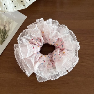 Close-up of pink floral scrunchie with layered white lace edges on dark wood background