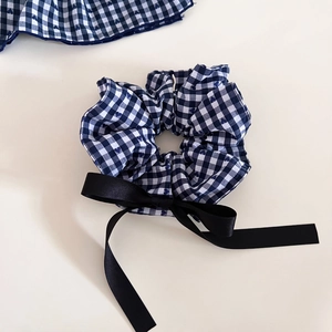 Detail view of blue gingham scrunchie with long black satin ribbon bow on white surface