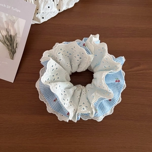 Detail of blue plaid hair scrunchie with cherry print and white lace layering on wood table