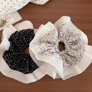 Close-up of black and white paisley pattern scrunchies with sheer ruffled edges on wood