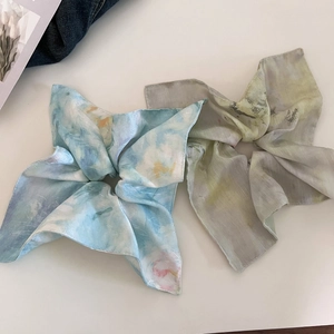 Detail view of two elegant silk-style scrunchies with blue and green floral prints