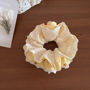 Detail of yellow plaid scrunchie with red cherry prints and white lace edges on wood