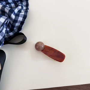 Detail of retro amber acetate hair clip with pink bead accent on checkered fabric